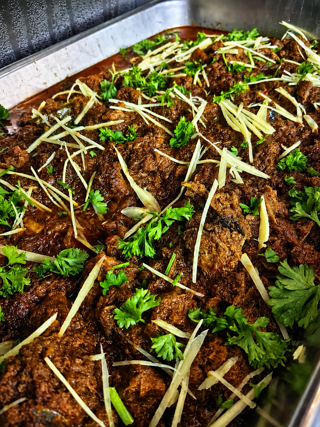 Dark slow-cooked meat in a serving tray, scattered with shredded ginger and coriander leaves.