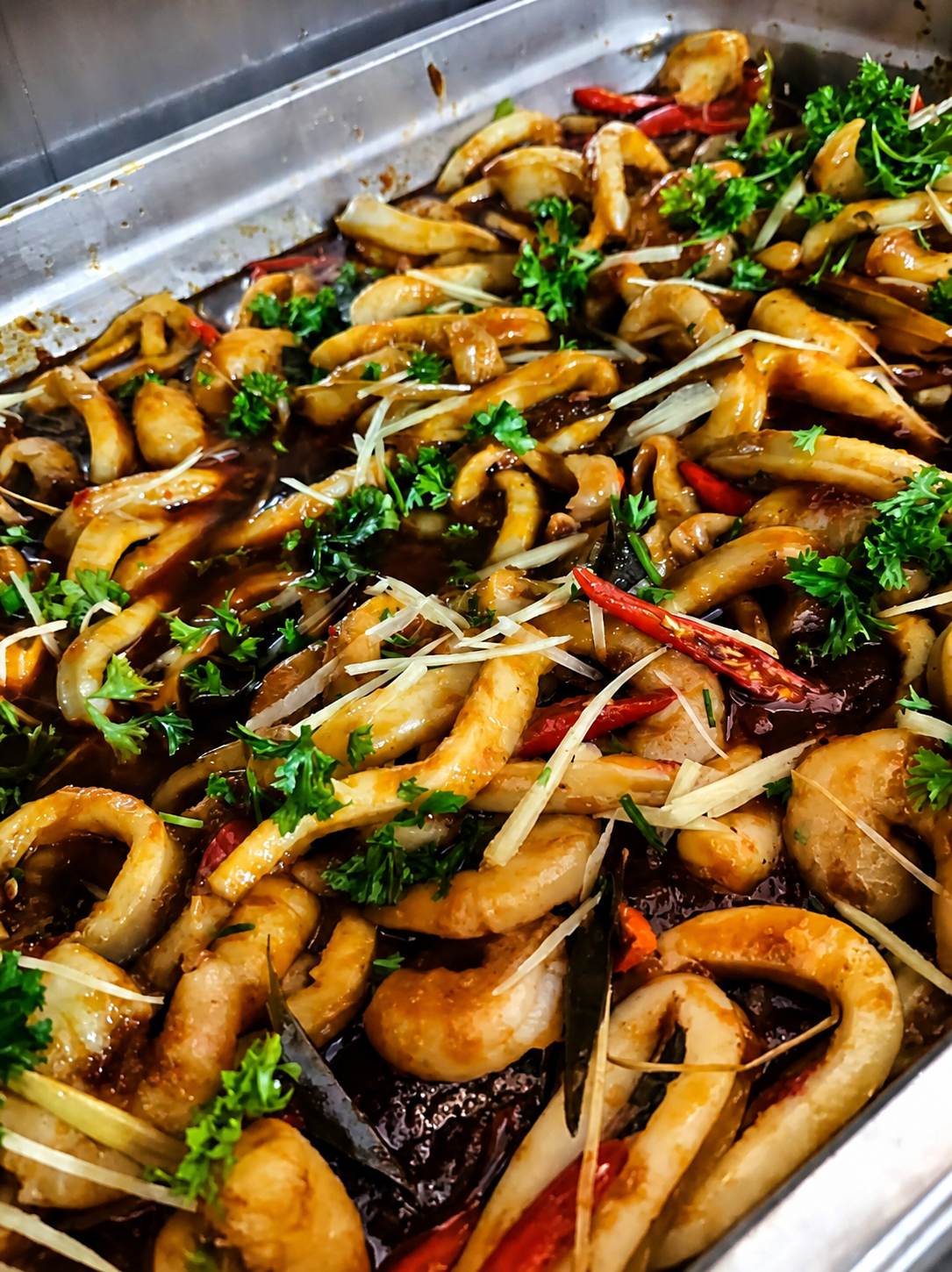 Squid rings in a dark chilli sauce with dried chillies, onion and shredded ginger in a serving tray.