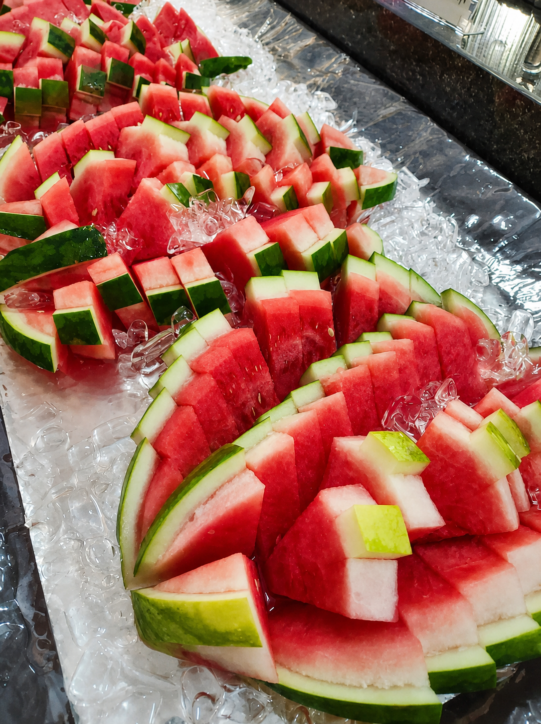 Cut watermelon arranged in overlapping rows on crushed ice.