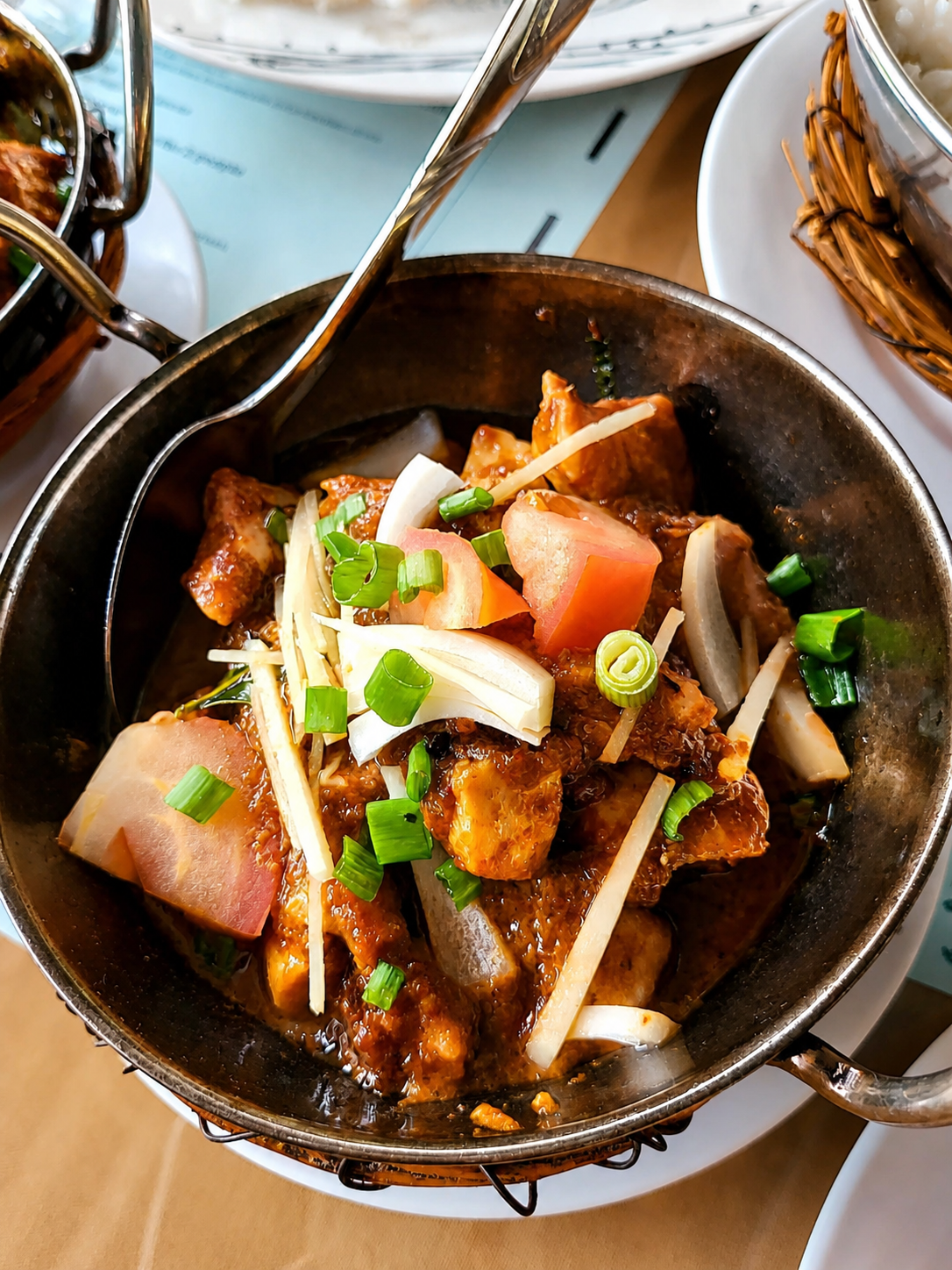 A karahi of dark curry with tomato and onion, topped with shredded ginger and spring onion.