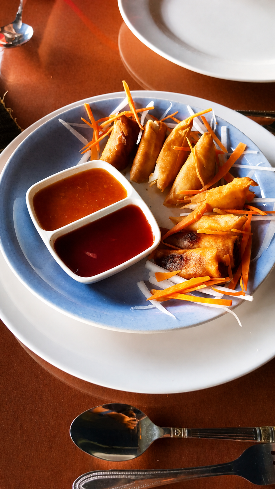 Spring rolls and samosas on a plate with two dipping sauces and shredded carrot.