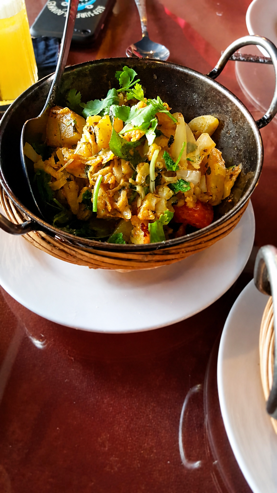 A dry stir-fry of cabbage, potato and tomato under fresh coriander, in a karahi set in a wicker holder.