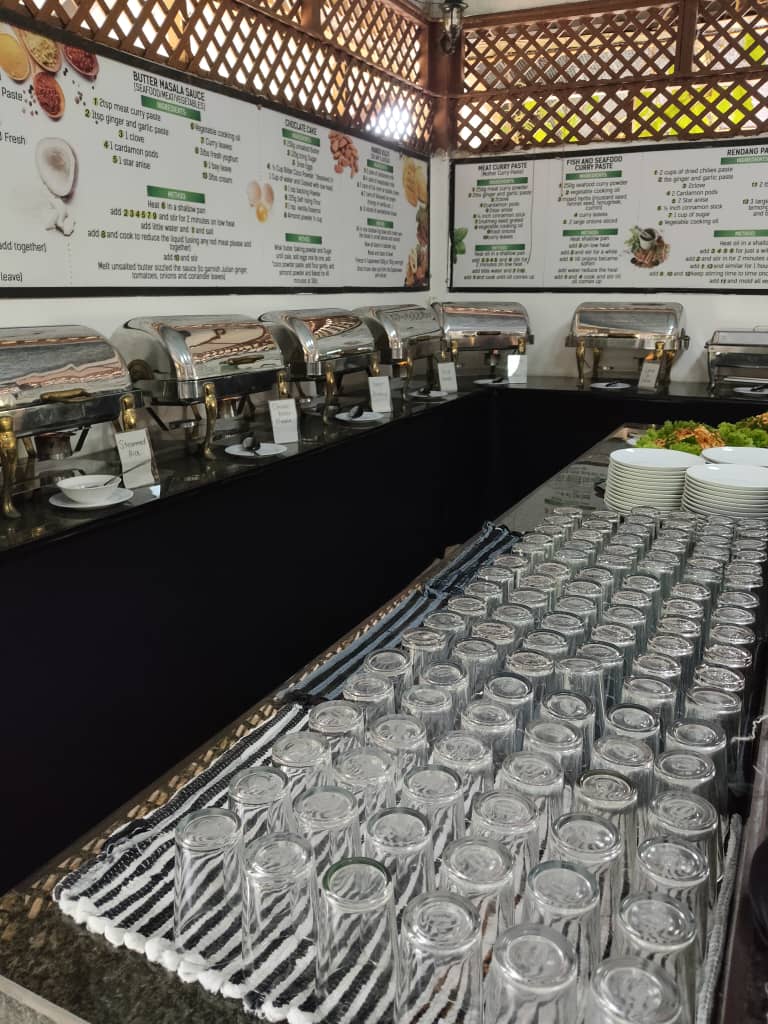 Rows of upturned glasses laid out along a counter beside a line of covered chafing dishes.